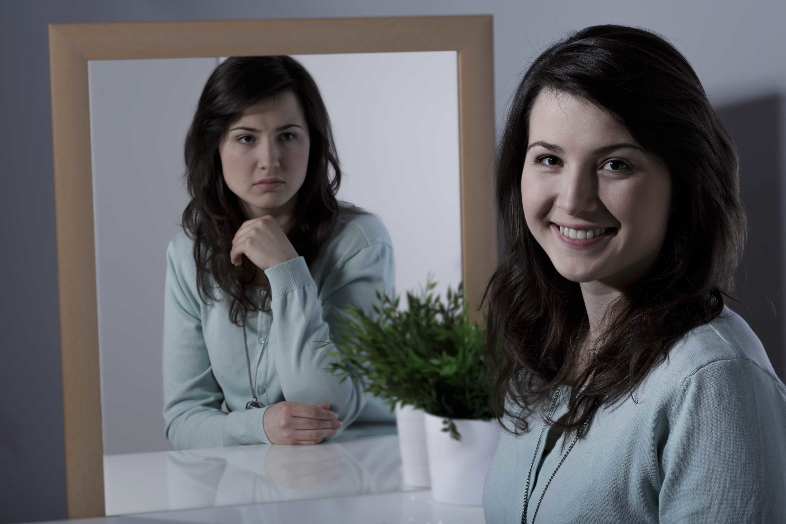 happy woman looking at depressed reflection of herself