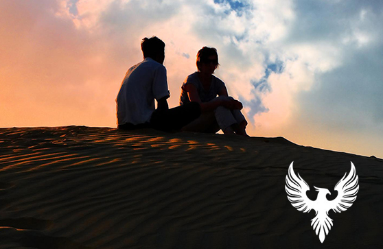 Two people on sand dune conversing at sunset