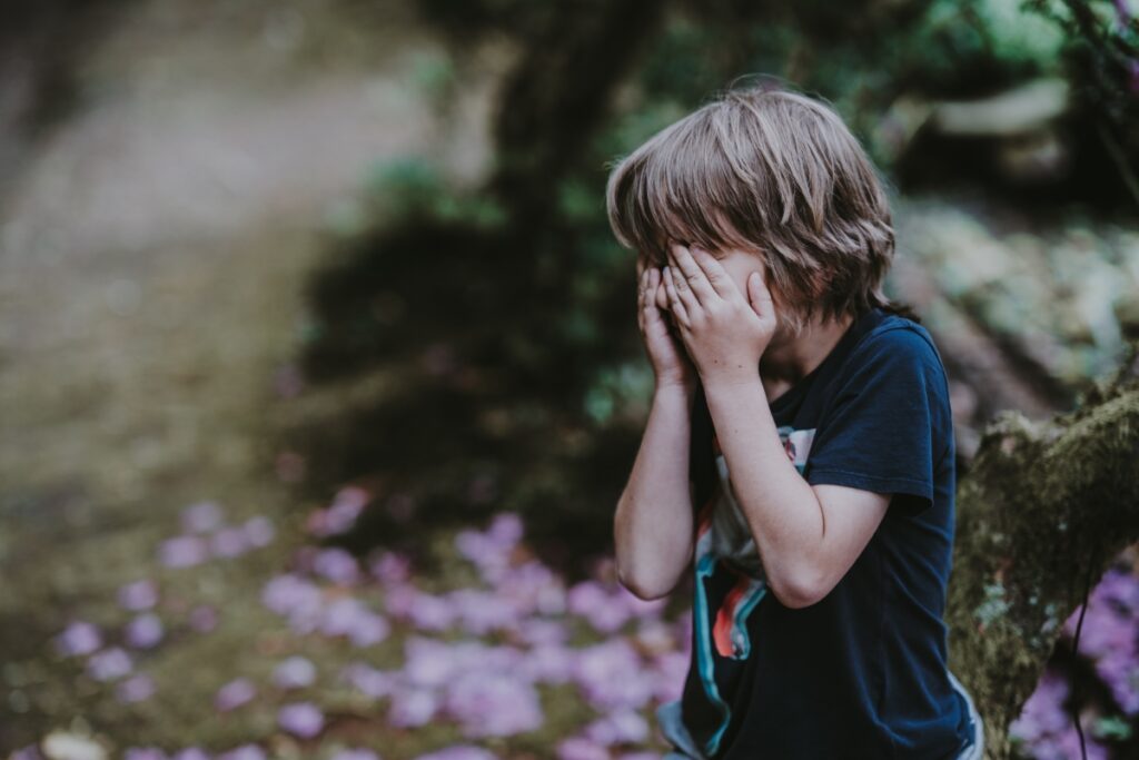 Young boy covering his face after experiencing childhood trauma
